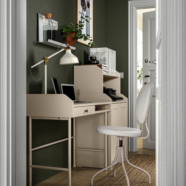 Home office setup with white desk, adjustable lamp, potted plant, laptop, and chair against green wall.