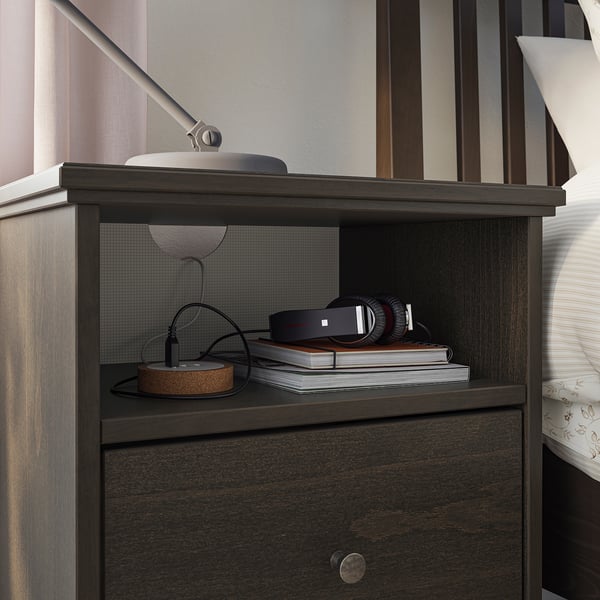 Dark wood bedside table with open shelf holding stack of books, headphones, and a lamp.