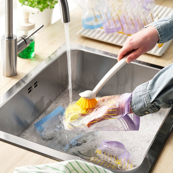 Person cleaning reusable, leakproof storage bags under a sink tap.