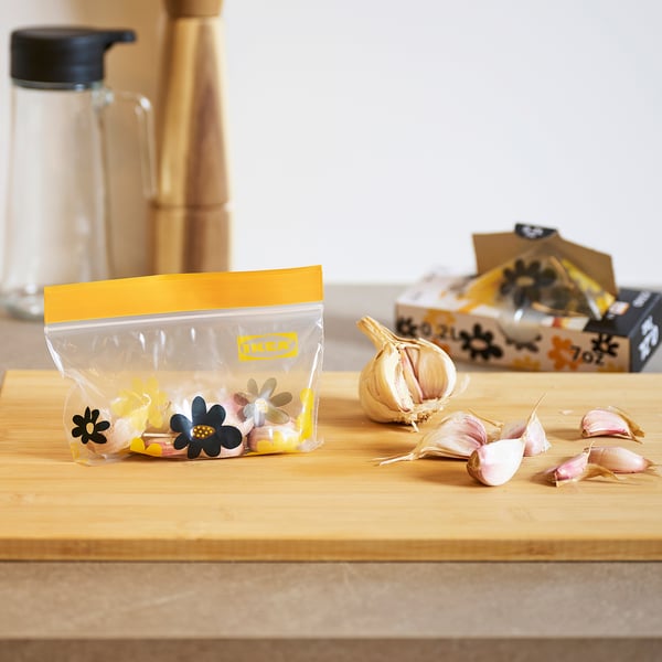 Garlic in yellow bag with floral designs on wooden board.