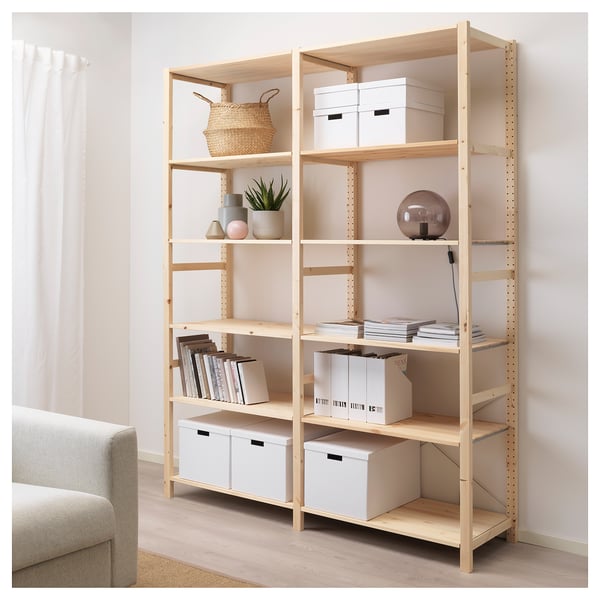 Wooden IVAR bookshelf with storage boxes, books, and decor near a couch and curtains.
