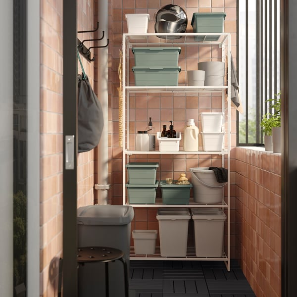 JOSTEIN white shelving unit with grey and green storage bins, bottles, and towels on metal hooks in tiled room.