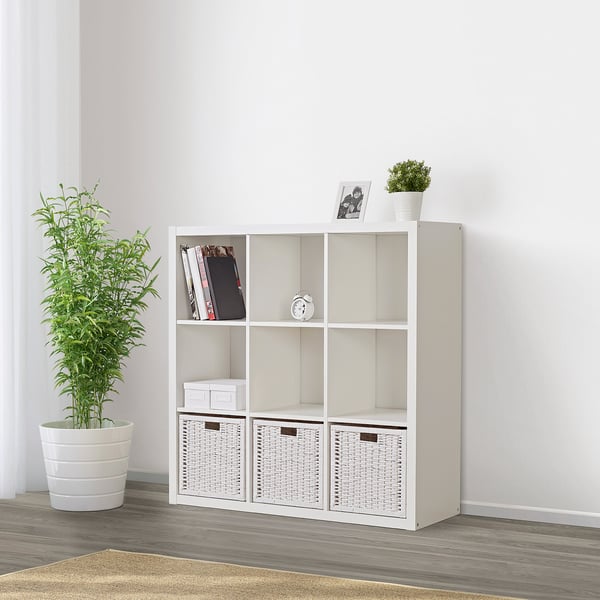 White KALLAX shelving unit withplant, books, bins, clock, and photo frame. Shows versatile storage and organisation.