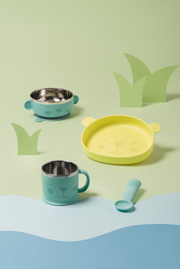 KANONKUL children’s set: green and yellow bear-themed mug, bowl, and sippy cup on pastel background.