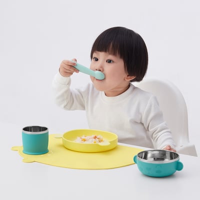 Child eating from KANONKUL plate, independently with guided shape. Teal spoon, stainless bowls.