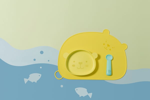 Yellow bear-shaped kids plate with blue spoon on pastel water background. Made of bpa-free plastic.