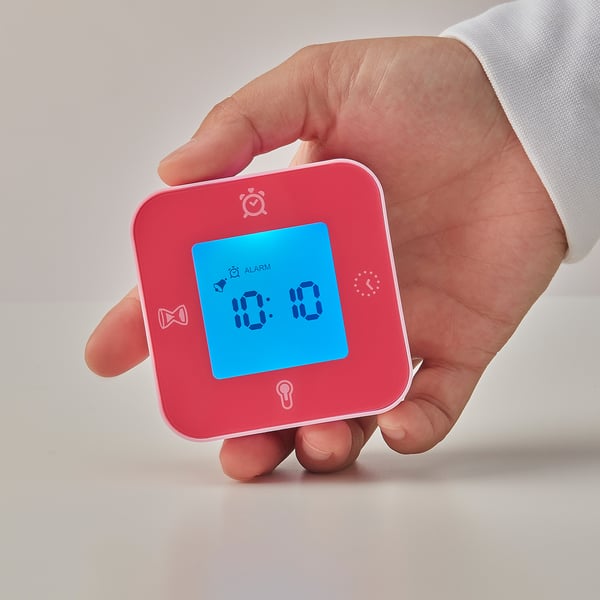 Person holding pink ikea KLOCKIS alarm clock, displaying blue screen with time 10:08.