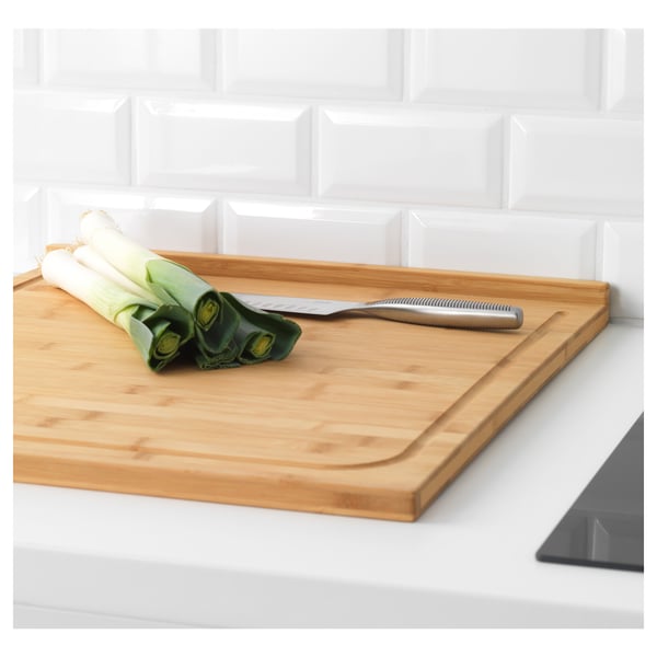 Wooden cutting board with knife and leeks, set on a white countertop.