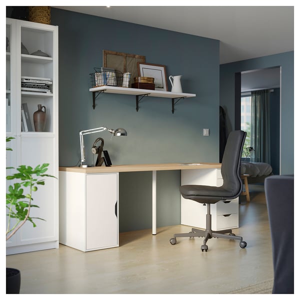 Spacious white home office desk with built-in shelves, wooden top, and a grey chair against green wall. Modern and minimalist design.