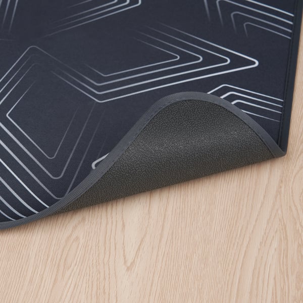 Dark gaming chair mat with geometric design, textured underside for grip, on wooden floor.
