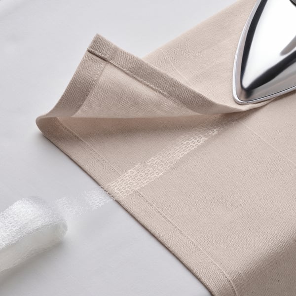 Beige curtain with tape lies on white surface, iron, hem tape, ready for hanging.