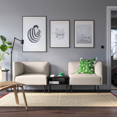 Modern living room with 2 beige sofas, art, 2 side tables, lamp, plant, large patterned rug.