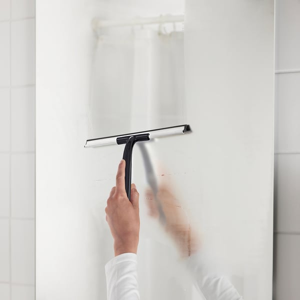 Person cleaning glass with black squeegee in white bathroom.