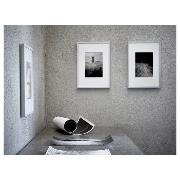 Three framed photos hang on a grey wall, below them sits a curved sculpture on a concrete floor.