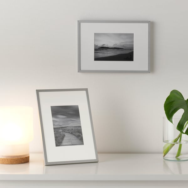 Black-and-white photo frames on a shelf. One frame stands upright, the other hangs on the wall.