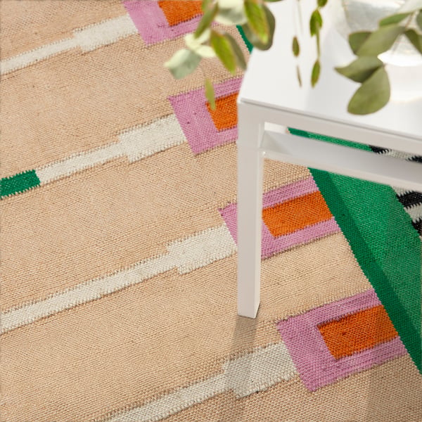 Colourful, handwoven jute rug with wool accents, ideal for living rooms, placed near a white table with a green plant.