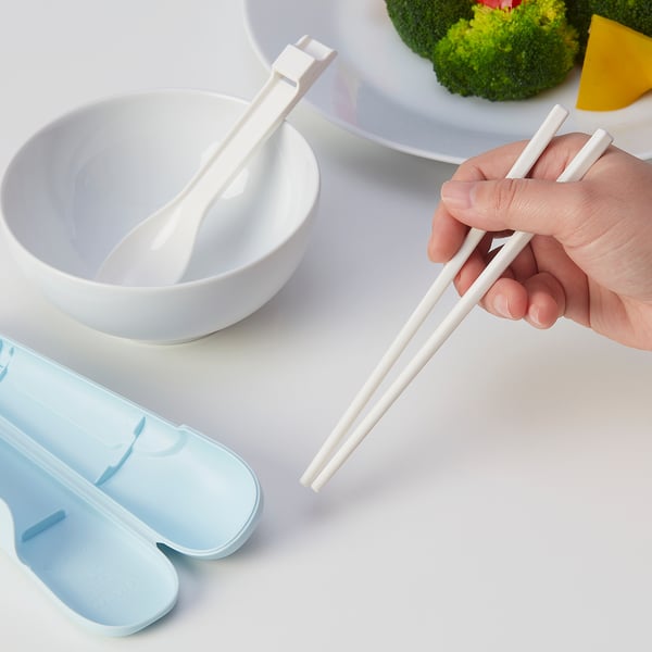 Hand holding white MIDDAGSGÄST chopsticks near small bowls and light blue case, ideal for travel.