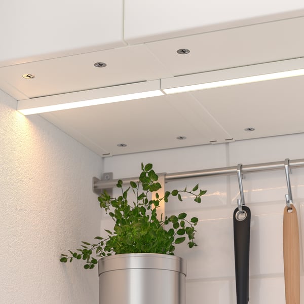 Modern kitchen with integrated led lighting under cabinets, illuminating the workspace. A potted plant sits beside hanging utensils.
