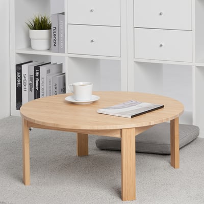 Bamboo coffee table with foldable legs, cup, and magazine. Near white shelf with books and plant.