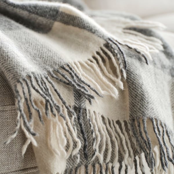 Close-up of cosy, textured wool blanket with fringe; light grey with dark stripes.