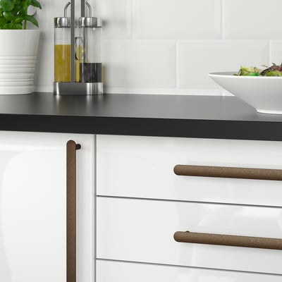 Modern kitchen with white cabinets, black countertop, and silver knobs. Counter has oil bottles and a bowl.