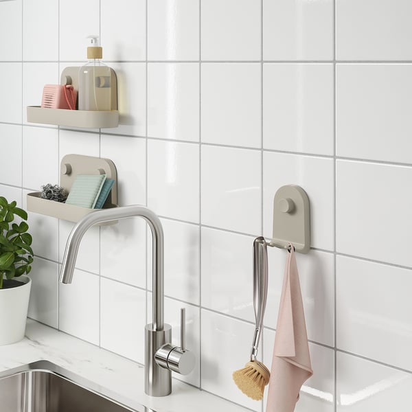 Kitchen sink with wall-mounted storage; towels and brush on hooks, soap dispenser on shelf; plant nearby.