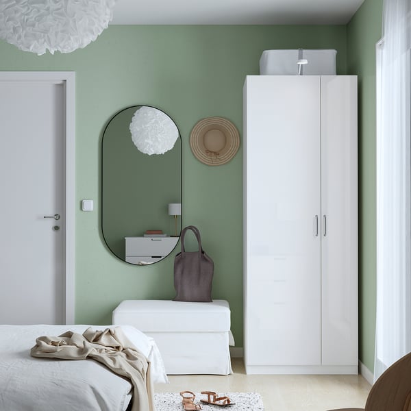 Minimalist bedroom with green walls, white PAX wardrobe, round mirror, and hanging hat. Wardrobe tall, narrow, with closed doors.