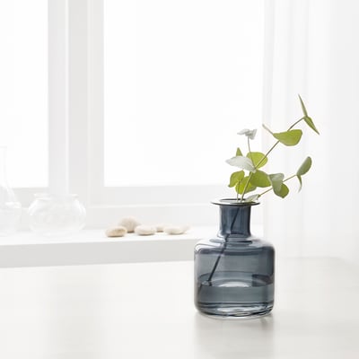 Small blue vase with twig, on white shelf by window.