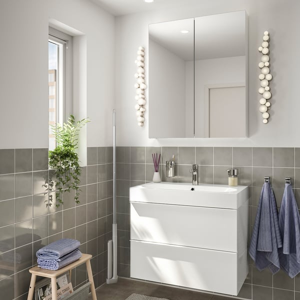 Modern bathroom with white sink, mirror, dark tiles. Blue towels hang and fold on stool with plant. White mop beside.