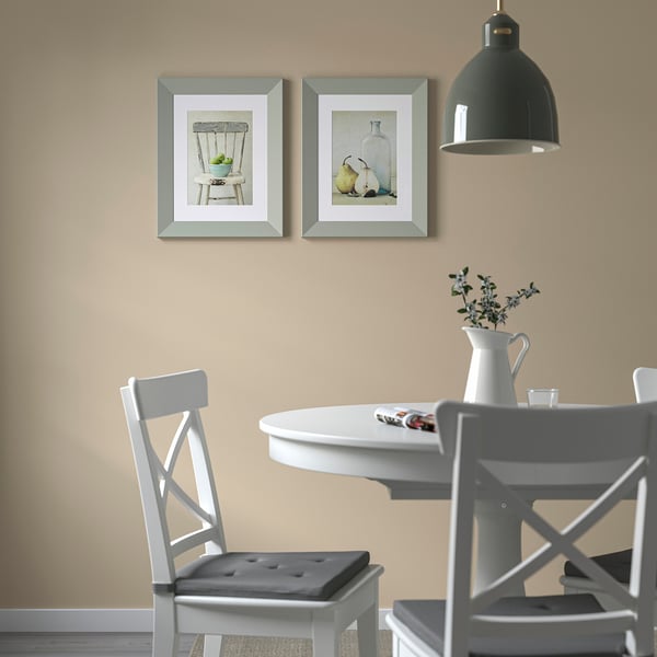 Still life paintings above dining table with white chairs and jug of flowers.