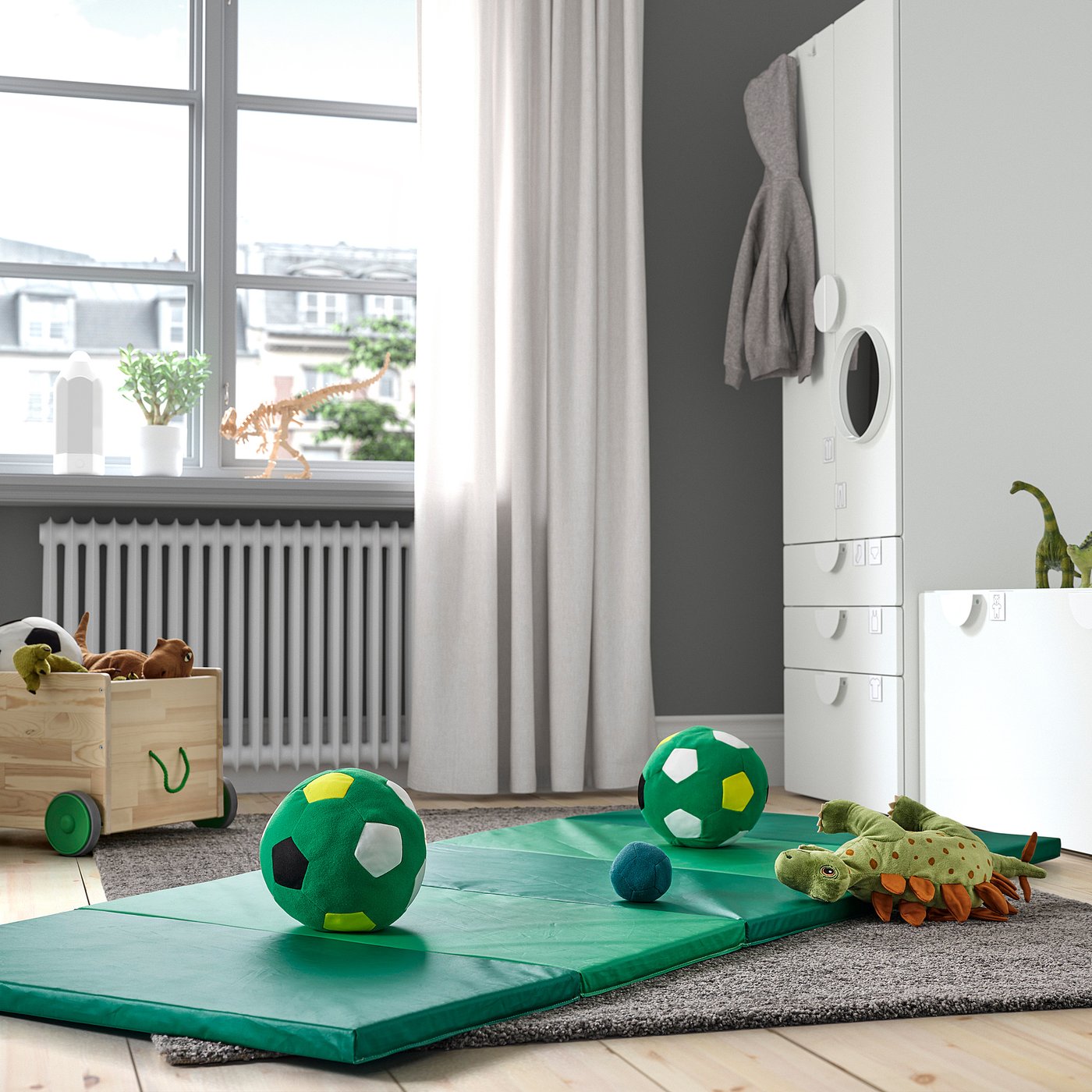 Playful kids room with folding green mats, plush toys, and a wooden bin. Mats are soft and padded, perfect for play.