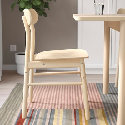 Wooden chair with rounded seat & back, near table. Warm, natural grains. Sturdy for home use.