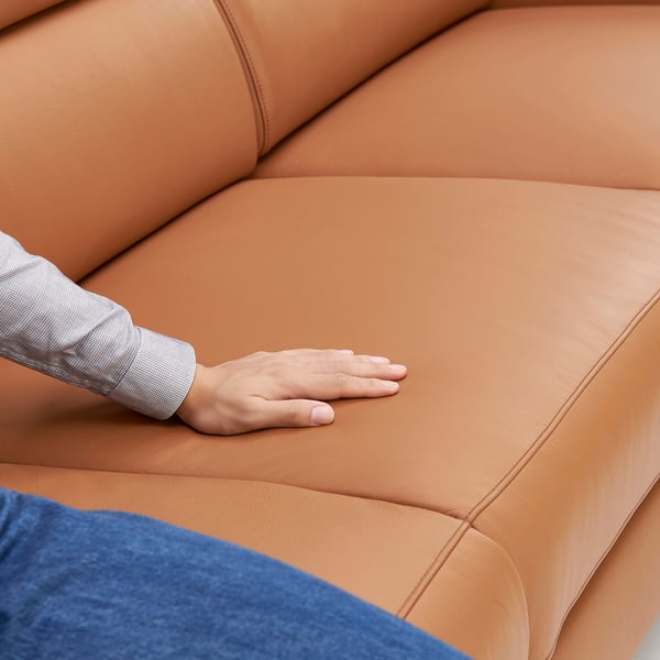 A hand touches high-quality, smooth leather on a modern sofa.