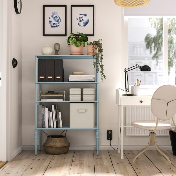 Blue SÅGMÄSTARE shelving unit near desk, holding books & plants, with adjustable feet.