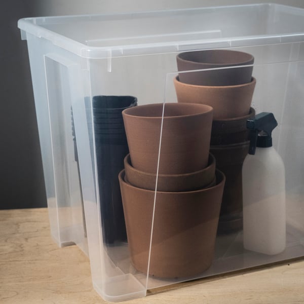 Clear plastic storage bin filled with brown terracotta pots and a spray bottle, neatly organised and visible through transparent walls.