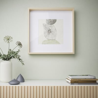 Framed minimalist art on light wall above wooden shelf with vases and books.