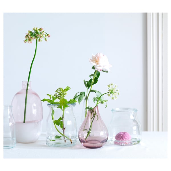 Six colourful vases with various flowers; includes pink, clear, curved, and round designs; placed near a window.