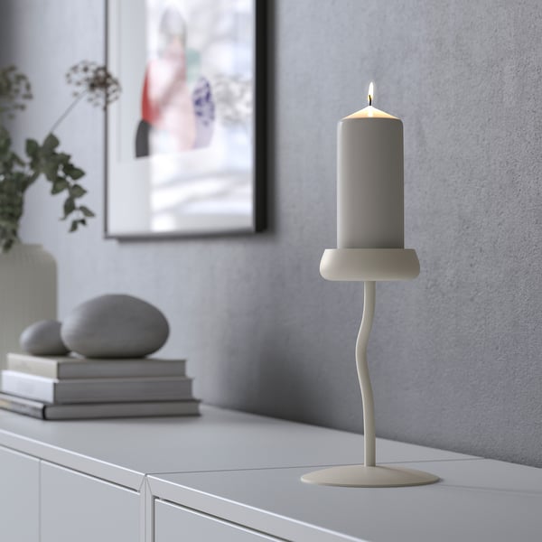 A grey candle in a decorative, flower-inspired stand on a cabinet. Relaxing light, stylish home decor.