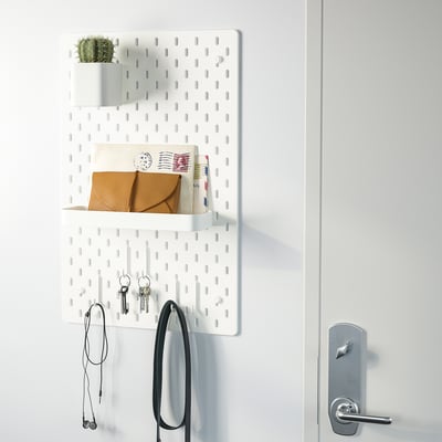 White wall organiser with shelves, hooks, and plant holder near a door.