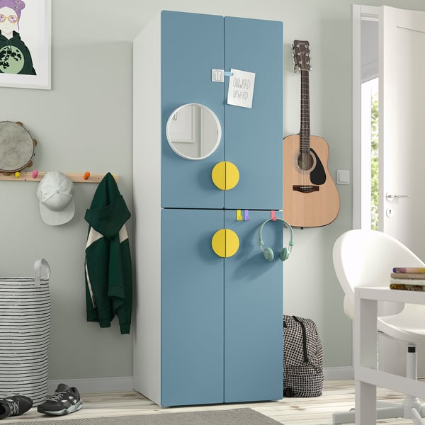 A blue SMÅSTAD wardrobe with round yellow doors, hanging a guitar and headphones, beside a white chair and a striped laundry basket.