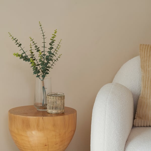 Clear vase with eucalyptus stems sits on round wooden table.