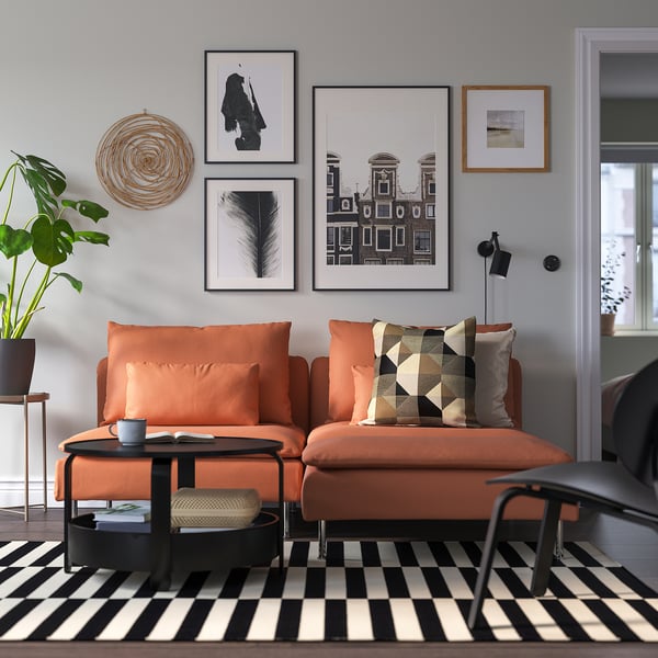 Modern living room with orange sectional sofa, art, black coffee table, striped rug, plant, black chair.