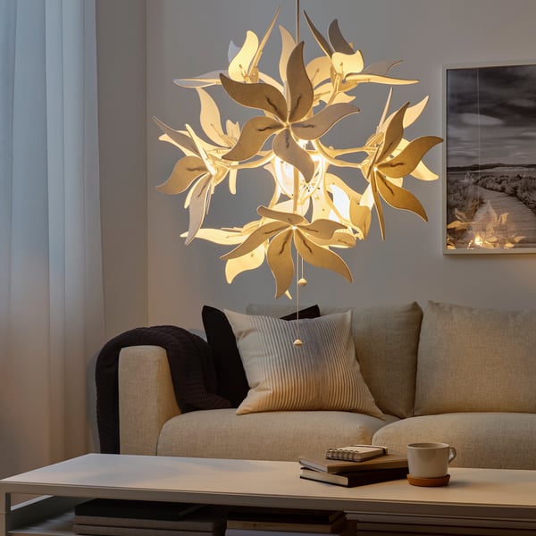 Unique hanging lamp with leaf design, warm light, above a beige couch with pillows.