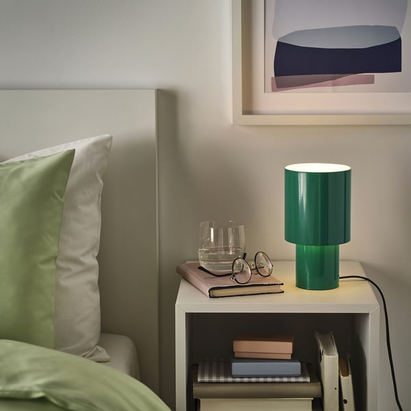 Green SPETSBOJ lamp on bedside table, lit softly, near bed & books.