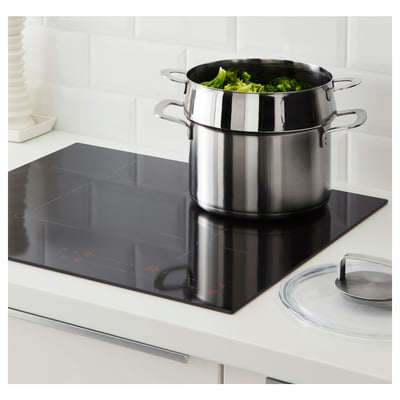 Stainless steamer on stove with green veggies.