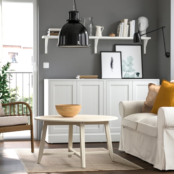 Modern living room with natural-tone rug, black stripes, wooden table, grey sofa, white cabinet, hanging black lamp, framed art, and a wooden bowl.