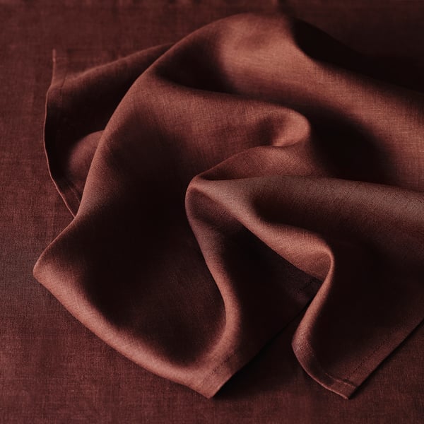 A closeup of rich, brown linen, showcasing its natural texture and subtle sheen. Folded neatly, highlighting its quality and absorbent nature.
