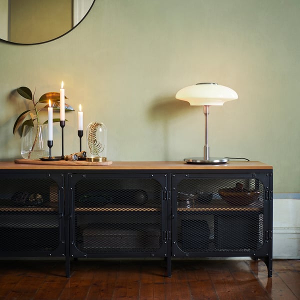 Industrial-style sideboard with metal mesh doors, candles, and a vintage-style lamp with a metallic base and white glass shade on top.