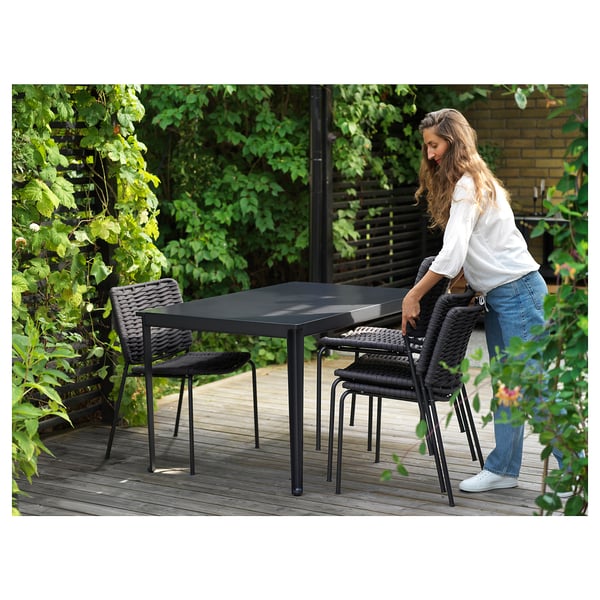 Person arranging black outdoor furniture set on a deck.