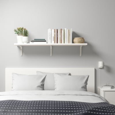 Modern bedroom with TOMTHULT shelf holding books & plants above bed with 3 pillows.